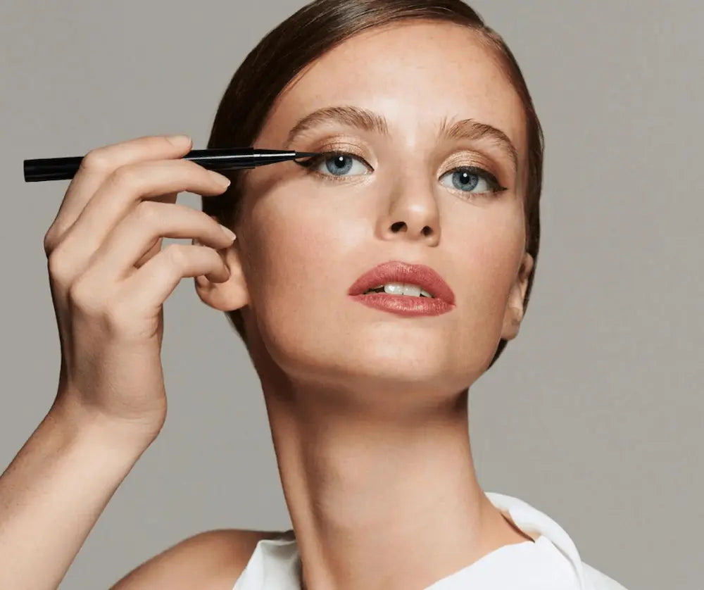 Frau trägt mit einem schlanken schwarzen Eyeliner-Pen einen feinen Lidstrich am oberen Augenlid auf, natürliches Make-up