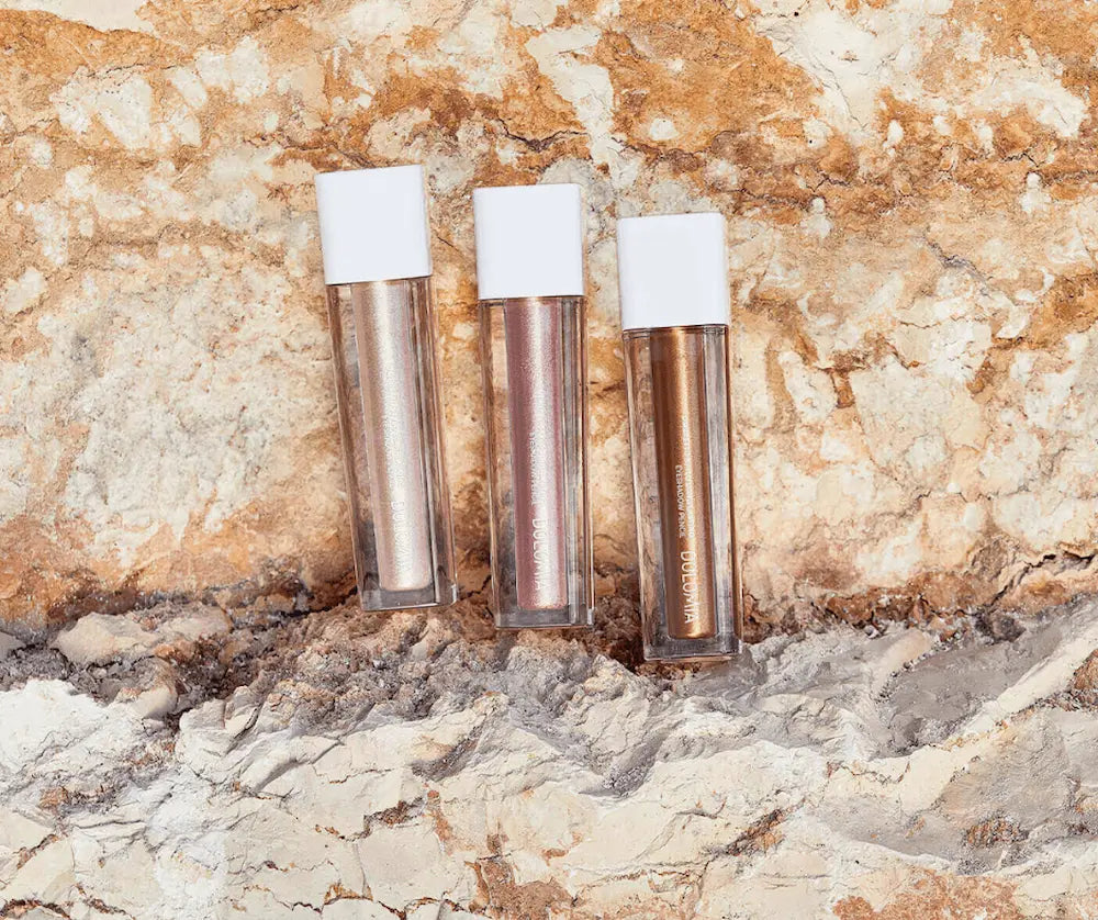 Drei flüssige Lidschatten von Dolomia mit weißen Kappen in Silber, Roségold und Bronze auf hellem Steinhintergrund