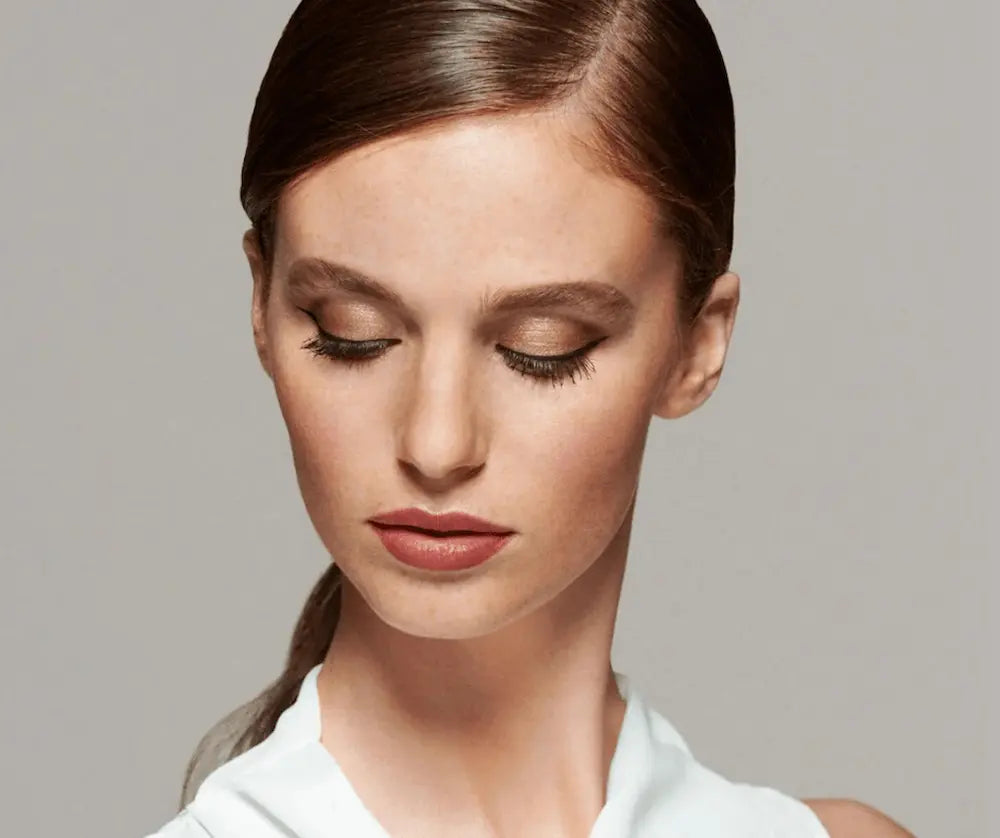 Model mit geschlossenen Augen, dezentem Lidschatten in Goldtönen, schwarzem Eyeliner und natürlichem Make-up im Portrait