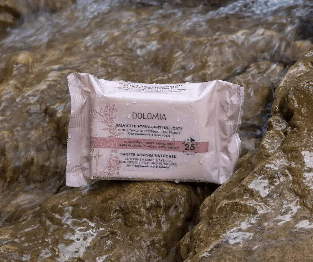 Dolomia Sanfte Abschminktücher in rosa Verpackung mit 25 Tüchern für empfindliche Haut, Augen, Lippen und Gesicht, auf nassen Felsen.