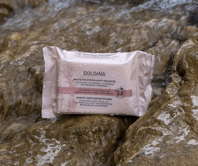 Dolomia Sanfte Abschminktücher in rosa Verpackung mit 25 Tüchern für empfindliche Haut, Augen, Lippen und Gesicht, auf nassen Felsen.