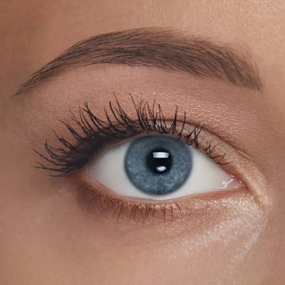 Nahaufnahme eines blauen Auges mit langen, geschwungenen Wimpern, betont durch schwarze Mascara und natürlich geformter Augenbraue.