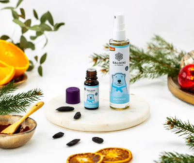 Baldini by Taoasis Winterzeit Naturduft als braune Tropfenflasche mit lila Deckel und Raumspray mit Eisbär-Motiv auf Marmorplatte, dekoriert mit Orangenscheiben und Tannenzweigen