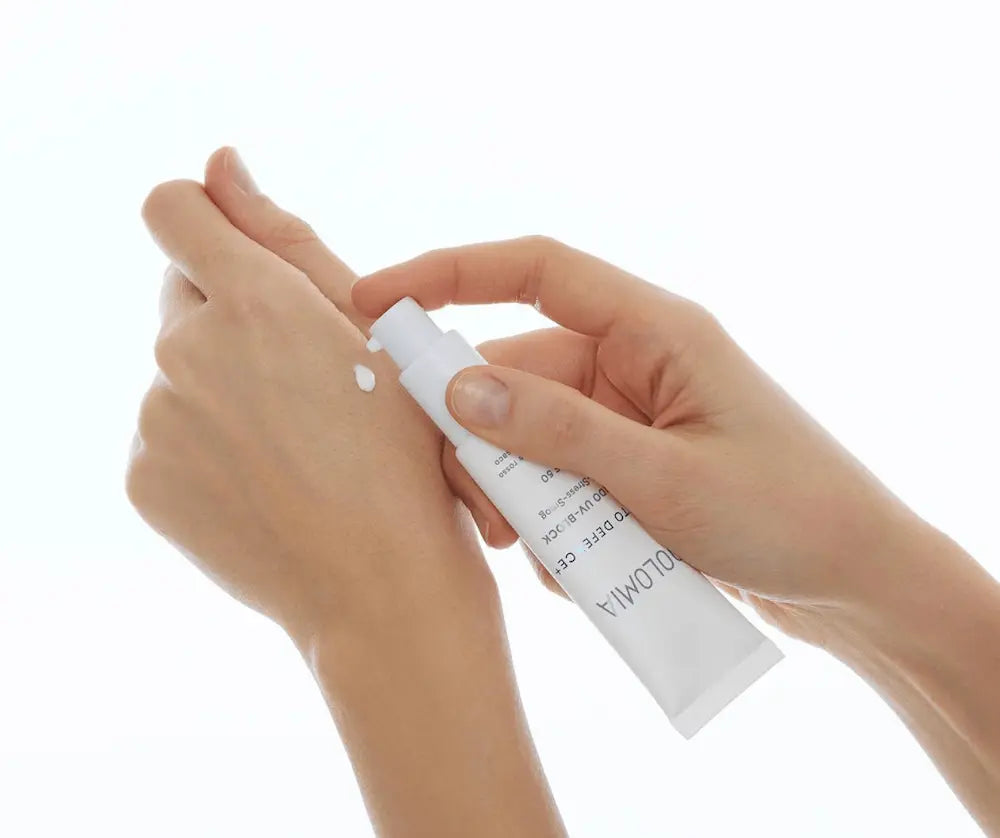 Hände tragen weiße Creme aus der Dolomia Fluido UV-B Block Tube auf den Handrücken auf, sichtbar SPF 60