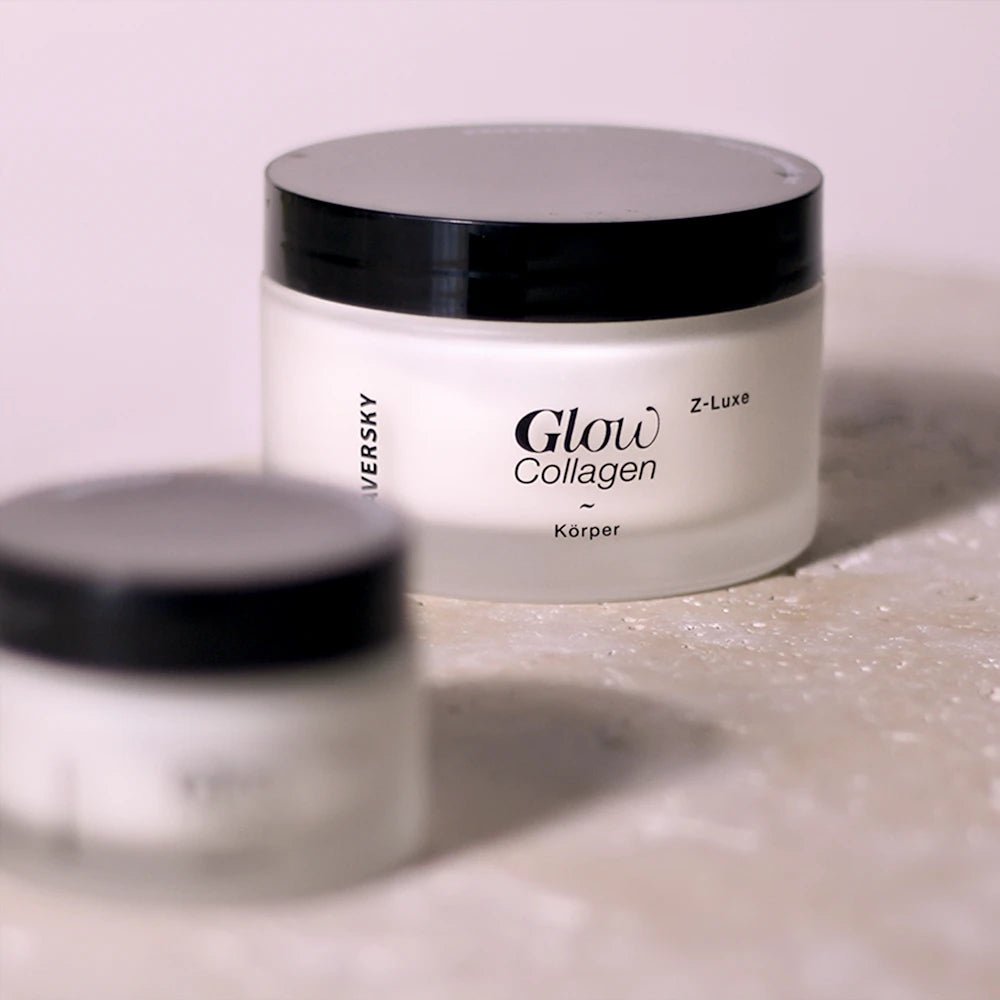 Weißer Cremetiegel Glow Collagen Körper Z-Luxe mit schwarzem Deckel auf hellem Steinuntergrund, zweiter Tiegel unscharf im Vordergrund