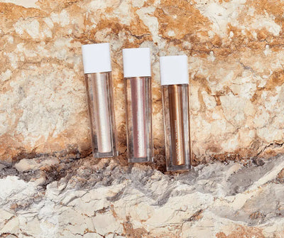 Drei flüssige Lidschatten von Dolomia mit weißen Kappen in Silber, Roségold und Bronze auf hellem Steinhintergrund