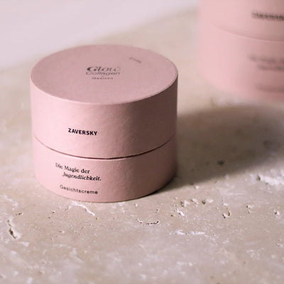 Runde rosa Verpackung der Zaversky Glow Collagen Gesichtscreme mit Aufschrift „Die Magie der Jugendlichkeit“ auf Steinoberfläche
