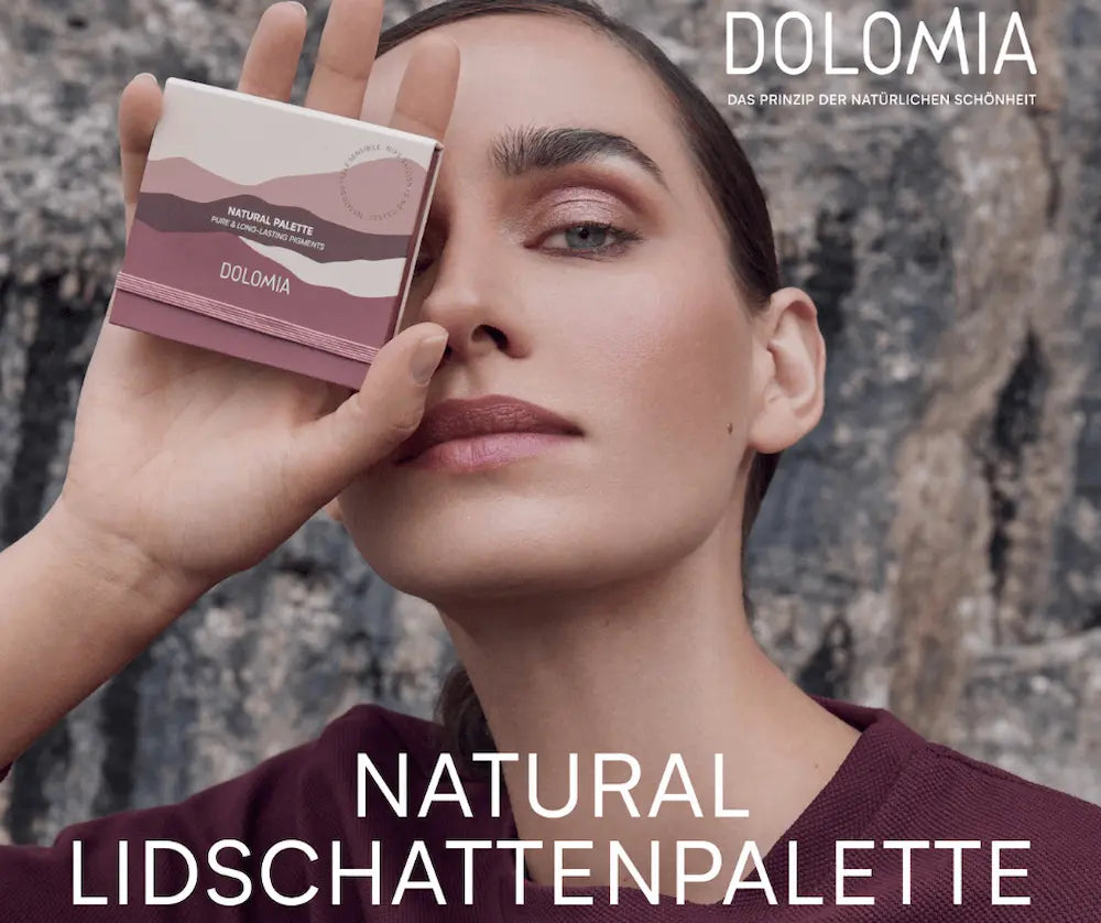 Model hält Dolomia Natural Palette Lidschattenpalette in Beere- und Rosatönen vor das Auge, dezentes Augen-Make-up sichtbar.