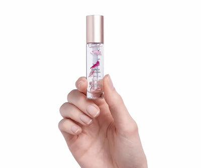 Hand hält transparentes Lippenpflegeöl Dolomia Flower Infusion Lip Care Oil mit Blütenblättern und roségoldenem Deckel
