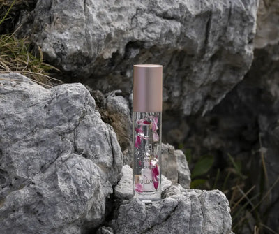 Dolomia Flower Infusion Lip Care Lippenpflegeöl in transparenter Flasche mit Rosenblüten und roségoldener Kappe auf Felsen