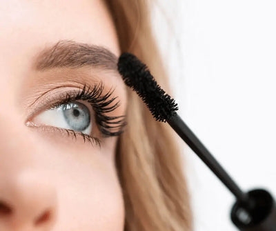 Nahaufnahme einer Frau mit blauen Augen, die schwarze Mascara mit voluminöser Bürste auf die Wimpern aufträgt.