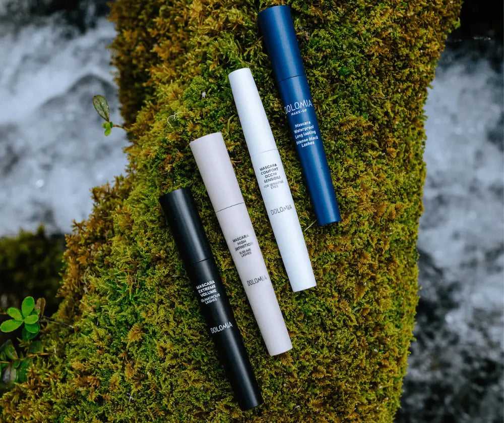 Vier Dolomia Mascaras in Schwarz, Beige, Weiß und Dunkelblau nebeneinander auf grünem Moos, Aufsicht im Naturmotiv.
