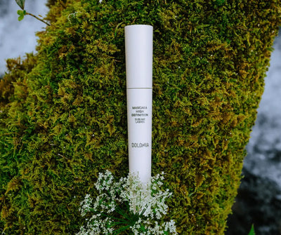 Weisse Mascara Dolomia High Definition Sublime Lashes vor grünem Moos mit weissen Wildblumen, naturnahe Produktaufnahme.