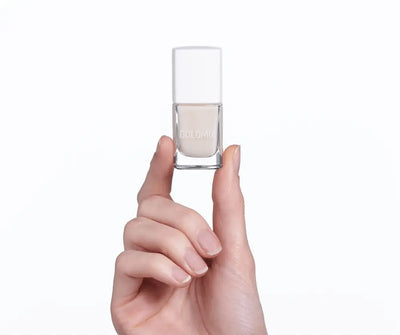 Hand hält ein kleines Nagellack-Fläschchen der Marke Dolomia mit weißem Deckel und hellem, transparentem Inhalt vor weißem Hintergrund.