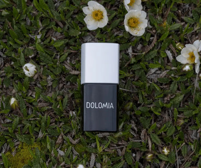 Dolomia Nagellackflasche mit schwarzem Glaskörper und weißem Deckel, liegend auf Moos mit weißen Blüten
