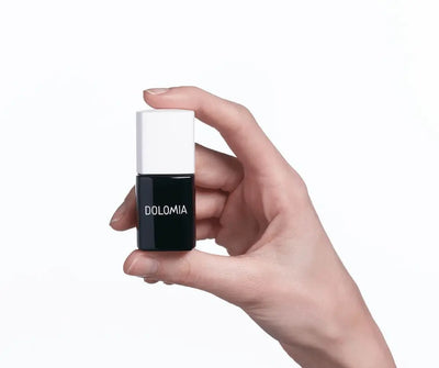 Hand hält kleine schwarze Nagellack-Flasche mit weißem Deckel und Aufschrift Dolomia vor weißem Hintergrund.