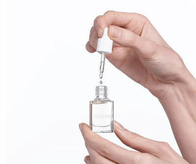 Hände halten transparente Dolomia Nagelpflegeöl-Flasche mit Pipette, ein Öltropfen fällt zurück in die geöffnete Glasflasche.
