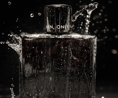 Dunkler Parfumflakon mit Aufschrift „Men, Only For" auf dem Verschluss, umgeben von Wassertropfen vor schwarzem Hintergrund