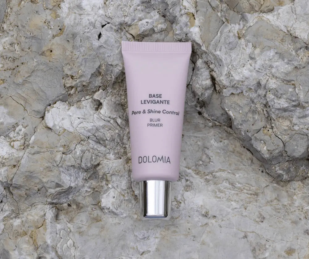 Dolomia Base Levigante Pore & Shine Control Blur Primer in flieder­farbener Tube mit silbernem Verschluss auf hellem Steinhintergrund.
