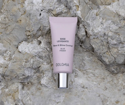 Dolomia Base Levigante Pore & Shine Control Blur Primer in flieder­farbener Tube mit silbernem Verschluss auf hellem Steinhintergrund.