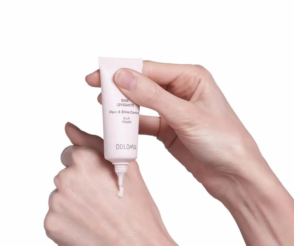 Hände halten rosafarbene Tube Dolomia Base Levigante Pore & Shine Control Blur Primer und tragen einen Tropfen auf den Handrücken auf.