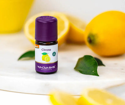 Taoasis Citrone Bio ätherisches Öl in brauner Glasflasche mit lila Verschluss, demeter- und Bio-Siegel, dekoriert mit frischen Zitronen